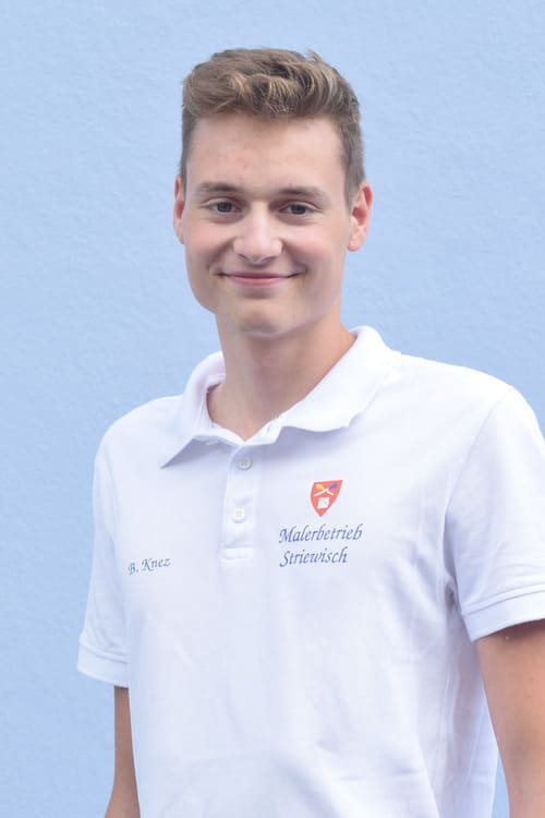 Mitarbeiter Bastian Knez, Portraitfoto ab der Hüfte, freundlich lächelnd